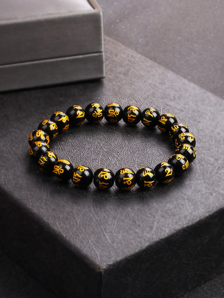 Black beaded bracelet with gold symbols on a dark surface