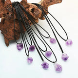 Necklaces with purple amethyst pendants hanging from a wooden block on a white background