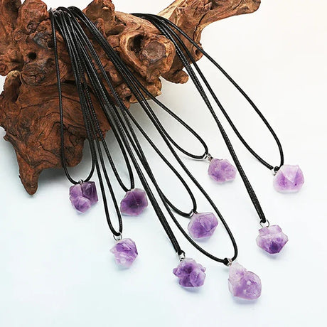 Necklaces with purple amethyst pendants hanging from a wooden block on a white background