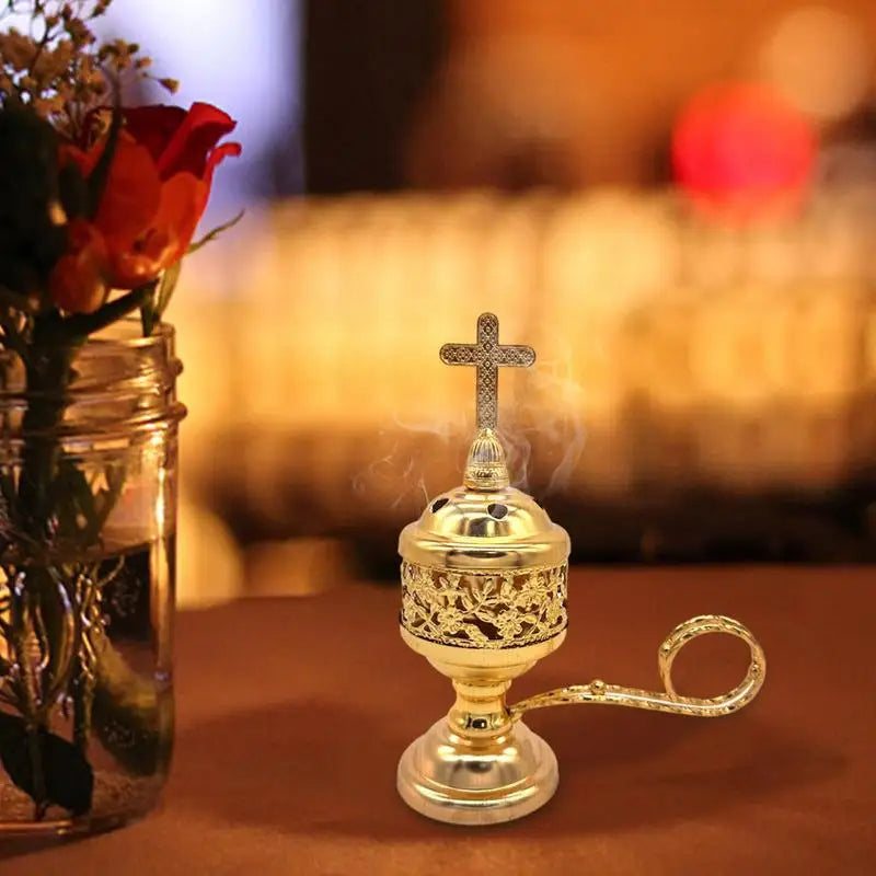 Gold incense burner with cross on top next to a vase of red roses.