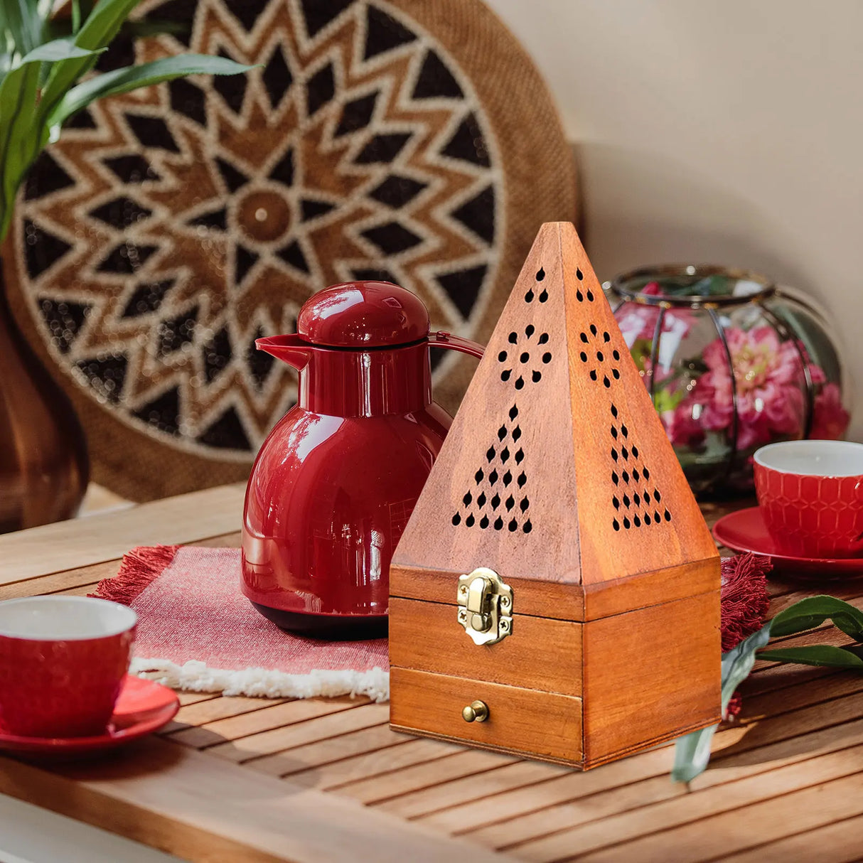 Red thermos and wooden pyramid-shaped lantern on a wooden surface with decorative elements.