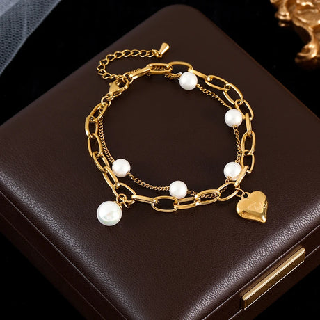 Gold bracelet with pearls and a heart charm on a dark surface