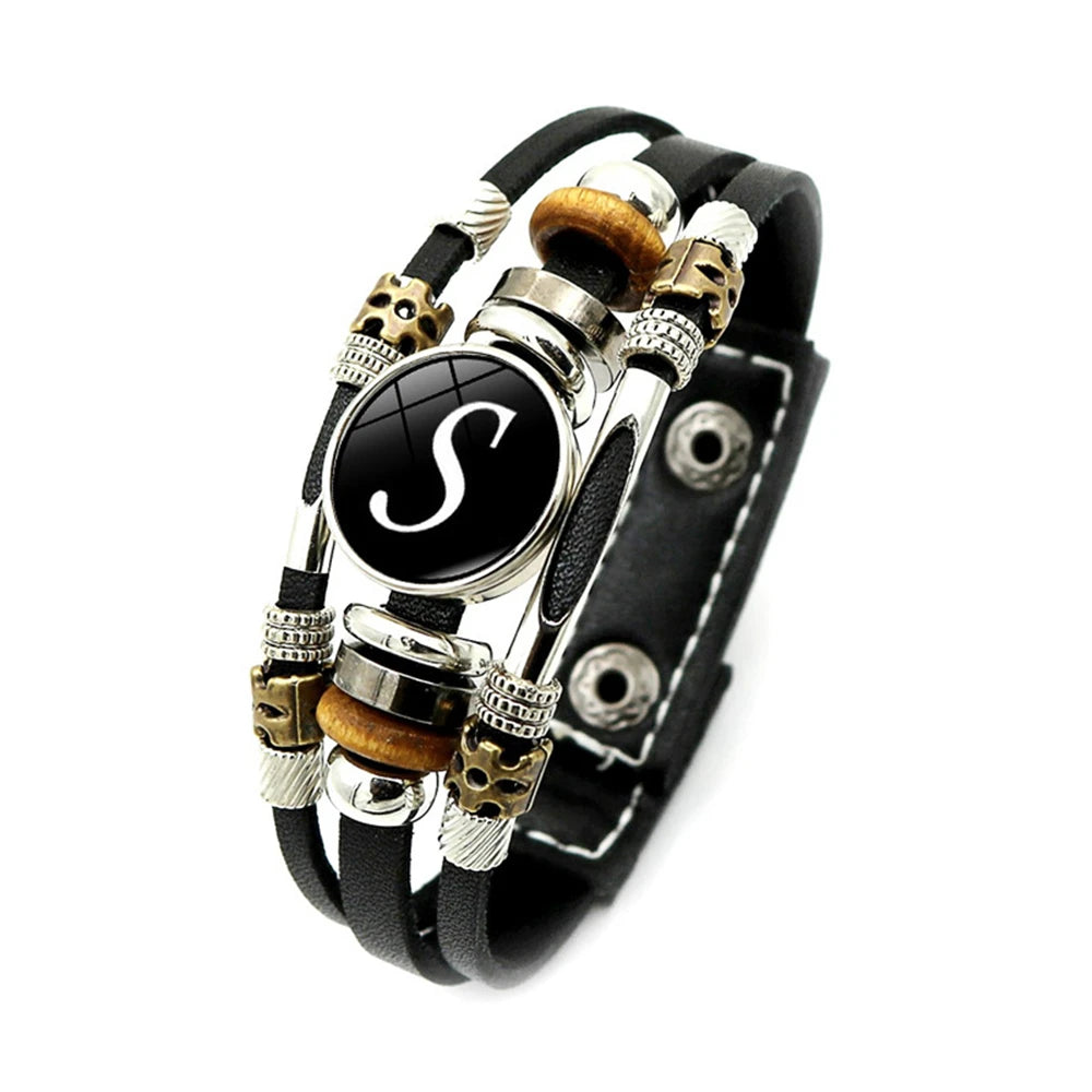Black leather bracelet with decorative beads and a central black circle with letter 'S'.