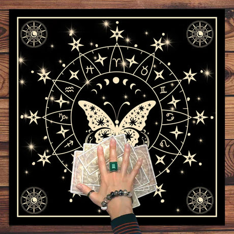 Butterfly design with tarot cards and hand holding a green gemstone on a black background with star and zodiac symbols.