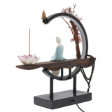 Decorative incense burner with a figurine, lotus flower, and cherry blossom branch on a white background