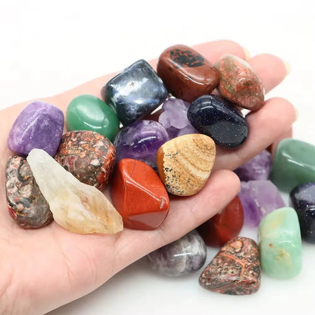 Hand holding a variety of colorful gemstones on a white background