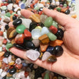 Hand holding a small pile of multicolored stones with a background of more stones.