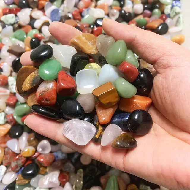 Hand holding a small pile of multicolored stones with a background of more stones.