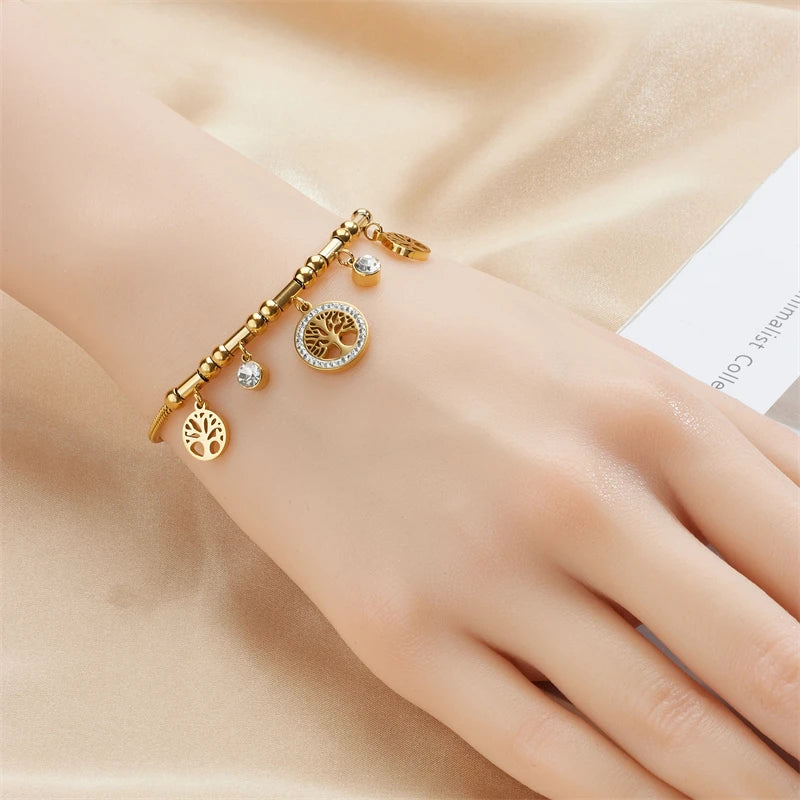 Gold bracelet with tree of life charm on a hand against a beige background