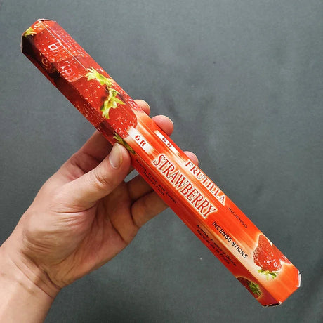 Hand holding a strawberry-flavored incense stick package against a gray background