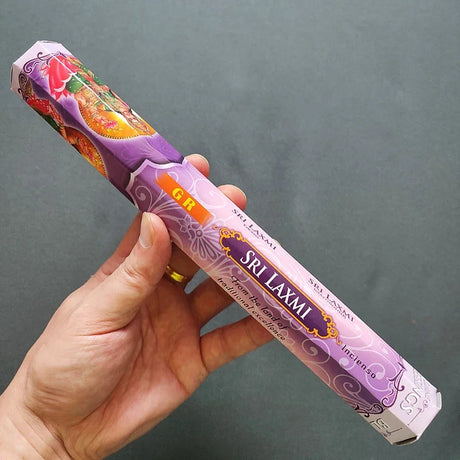 Hand holding a Sri Laxmi incense stick packaging against a gray background