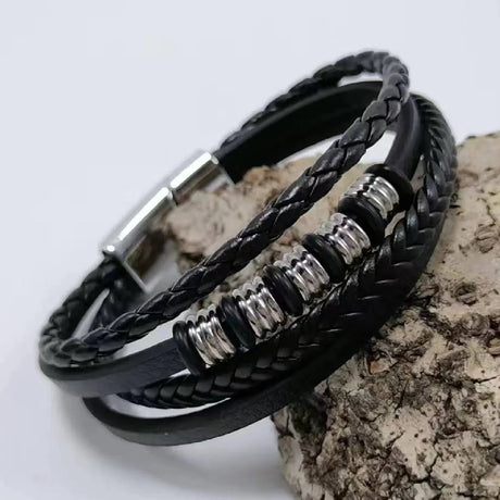 Black braided leather bracelet with silver accents on a textured surface