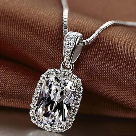 Silver necklace with a large, clear gemstone pendant on a brown fabric background