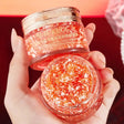 Two jars of KUGE cream held by a hand against a red background