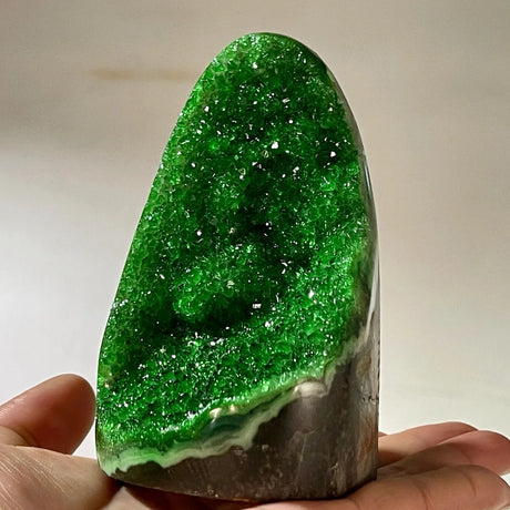 Green crystal rock held in hand against a neutral background