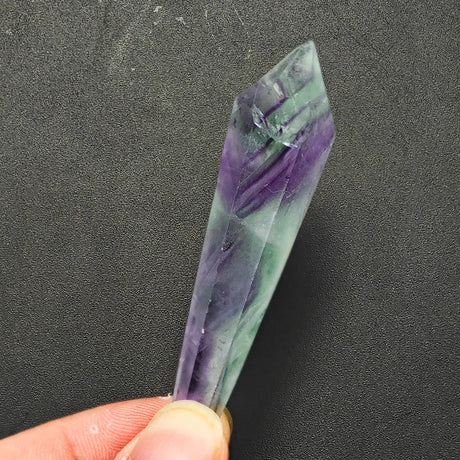 Clear crystal with purple and green hues held by a hand against a dark background