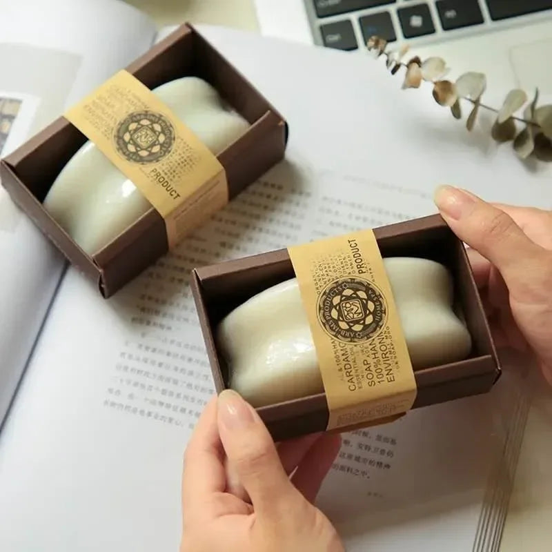 Bar of soap in a brown box with a decorative label, held by a hand on a white surface.