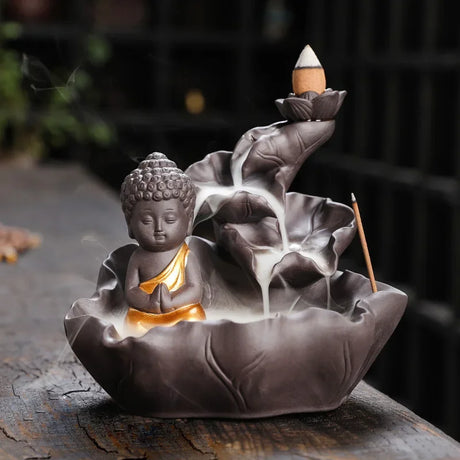 Decorative incense burner shaped like a Buddha figure with lotus flowers on a dark surface.