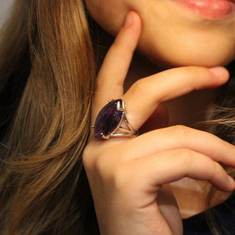 Close-up of a hand wearing a ring with a purple gemstone, touching hair.