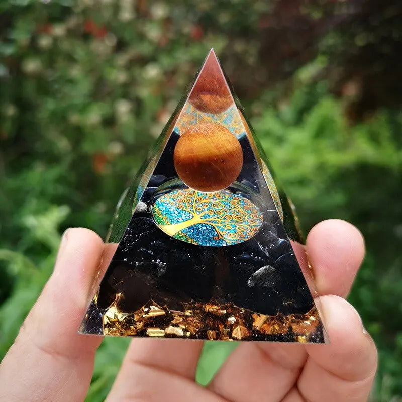 Triangular crystal with tree of life design held by a hand against a green leafy background