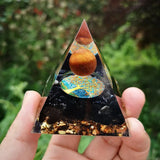 Triangular crystal with tree of life design held by a hand against a green leafy background