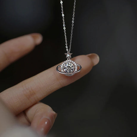 Silver necklace with a pendant held by a hand against a dark background