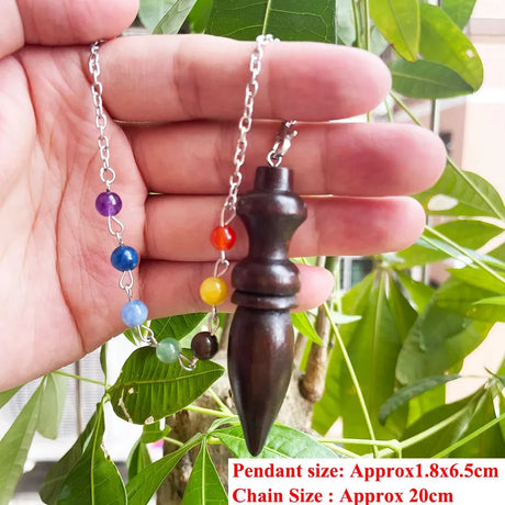 Hand holding a wooden pendant with colorful beads on a chain against a leafy background