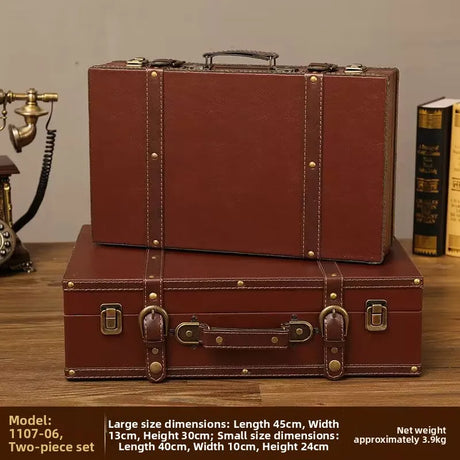Two vintage-style brown suitcases stacked on a wooden surface with a phone and book in the background.