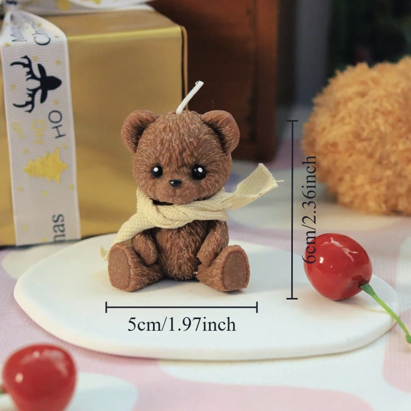 Small brown teddy bear with a yellow scarf on a white base, surrounded by cherries and a gift box.
