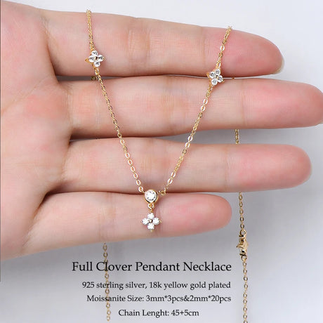 Gold necklace with clover pendants held in a hand against a white background