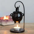 Black cauldron-shaped lamp with a lit candle on a wooden surface