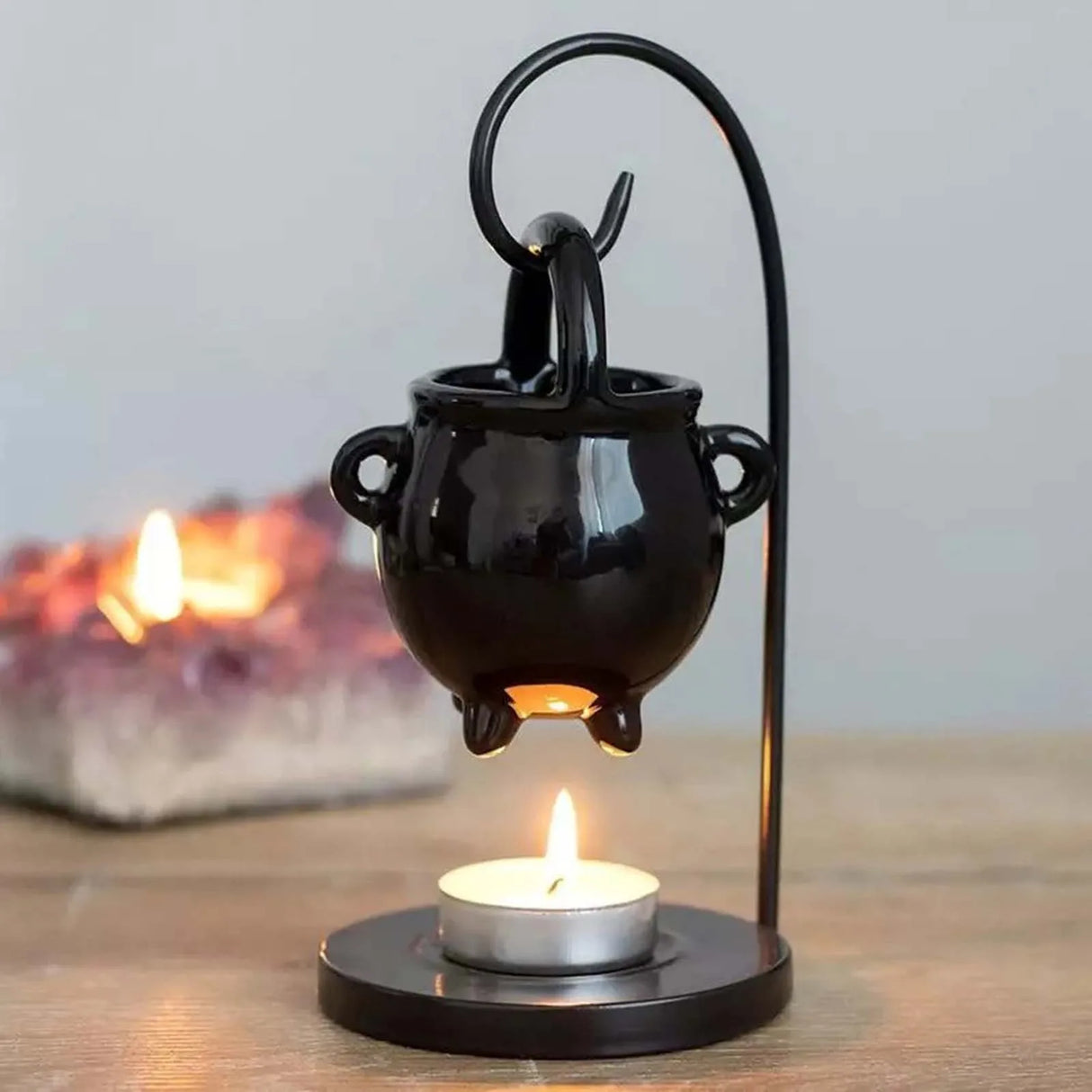 Black cauldron-shaped lamp with a lit candle on a wooden surface