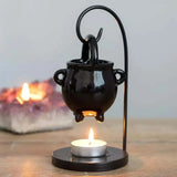 Black cauldron-shaped lamp with a lit candle on a wooden surface