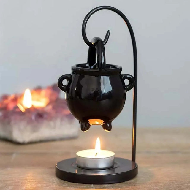 Black cauldron-shaped lamp with a lit candle on a wooden surface