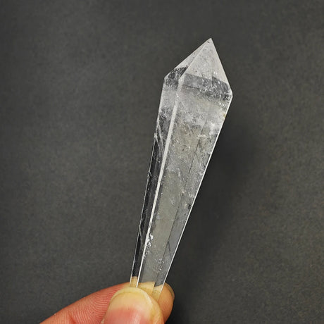 Clear crystal prism held by a hand against a dark background