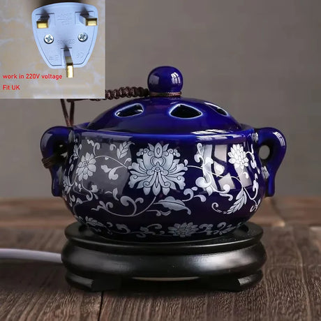 Blue floral-patterned ceramic warmer on a wooden surface with a voltage compatibility note.