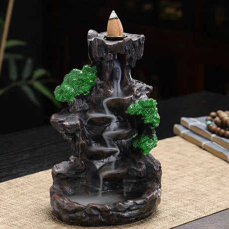 Decorative incense burner shaped like a mountain with greenery on a table.