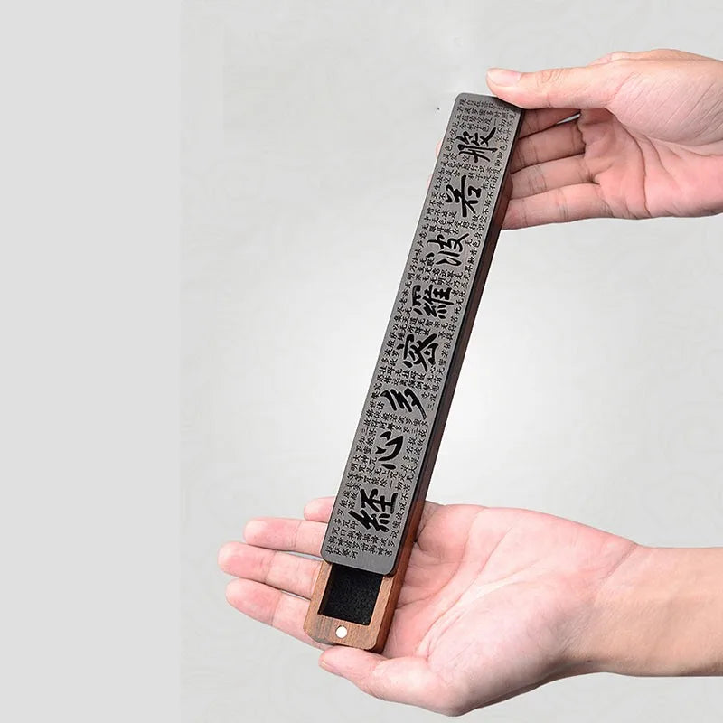 Hand holding a rectangular object with engraved text against a gray background