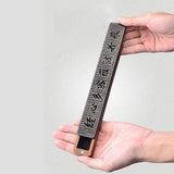 Hand holding a rectangular object with engraved text against a gray background