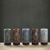 Five cylindrical decorative items with intricate patterns on a wooden surface and dark background