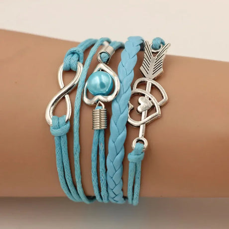 Turquoise braided bracelet with silver charms on a wrist against a neutral background