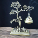 Decorative metal incense burner shaped like a tree with mountains on a dark background