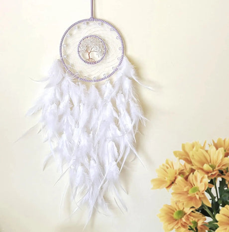 White dreamcatcher with feathers on a light background with yellow flowers.