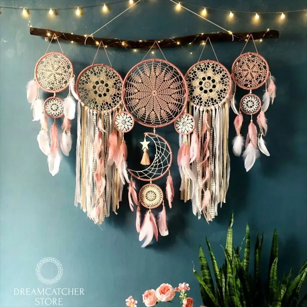 Set of dreamcatchers with feathers hanging against a teal wall with string lights.