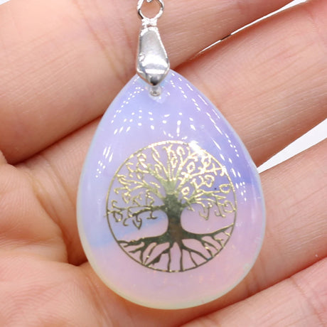 Teardrop-shaped pendant with tree of life design held in a hand