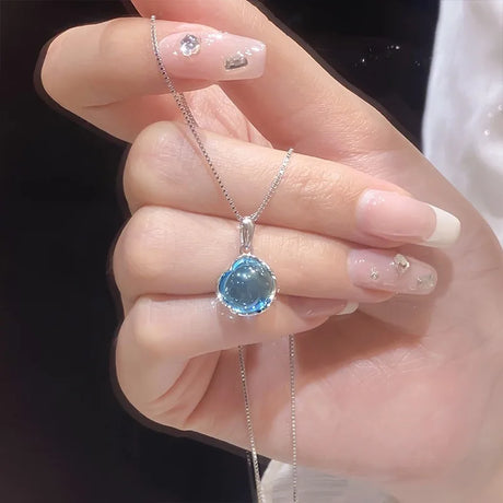 Hand holding a necklace with a blue pendant against a dark background