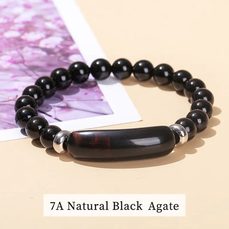 Black agate beaded bracelet on a beige surface with a pink floral background