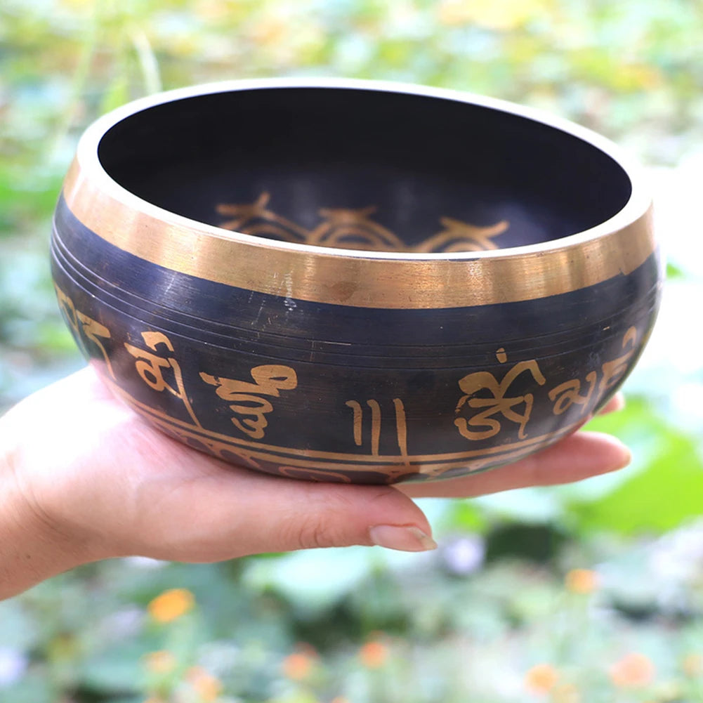Hand holding a black singing bowl with gold inscriptions against a blurred natural background