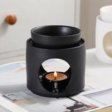 Black ceramic oil burner with a lit candle inside on a magazine