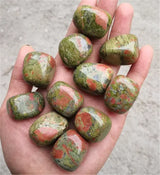 Hand holding a collection of green and red marbled stones against a neutral background